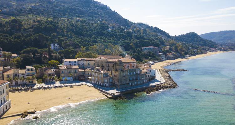 Luftaufnahme eines italienischen Küstendorfes mit schlossartigem Palast und Sandstrand neben türkisfarbenem Meer