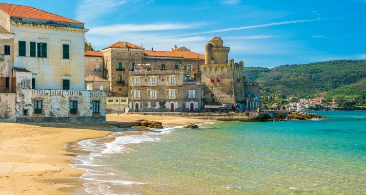 Farbenfrohe Küstendorf mit historischem Turm und sandigem Ufer unter hellem Himmel