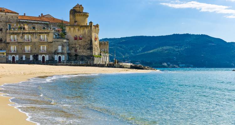 Goldener Sandstrand, der sich zu einem historischen Steinturm mit Hügeln im Hintergrund krümmt