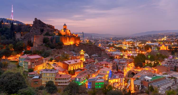 Twilight panorama of Tbilisi old town lights with Narikala fortress and colourful houses.