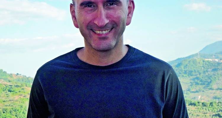 Smiling man with a mountainous landscape in the background.
