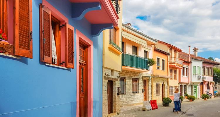 Bunt bemalte Häuser säumen eine schmale Straße, während eine Frau unter einem teilweise bewölkten Himmel spaziert