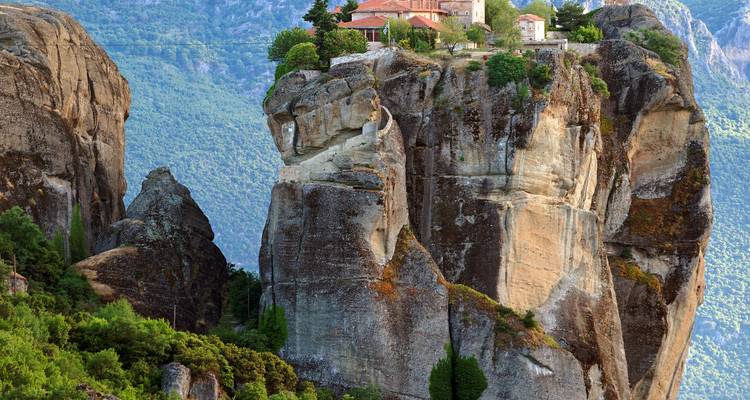 Ikonisches Meteora-Kloster, das auf einem hoch aufragenden Felspfeiler thront, umgeben von grünen Bergen