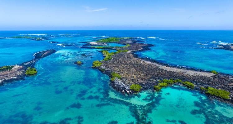 Vivid aerial shot of turquoise lagoons, black volcanic rock, and small islets in the Galapagos.