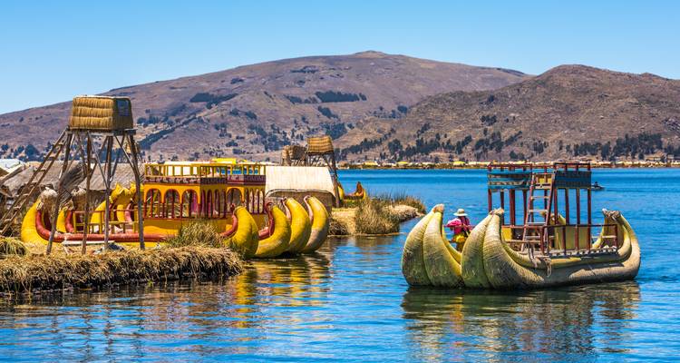 Colorful reed boats shaped like pumas floating on the blue waters of Lake Titicaca with hills behind.