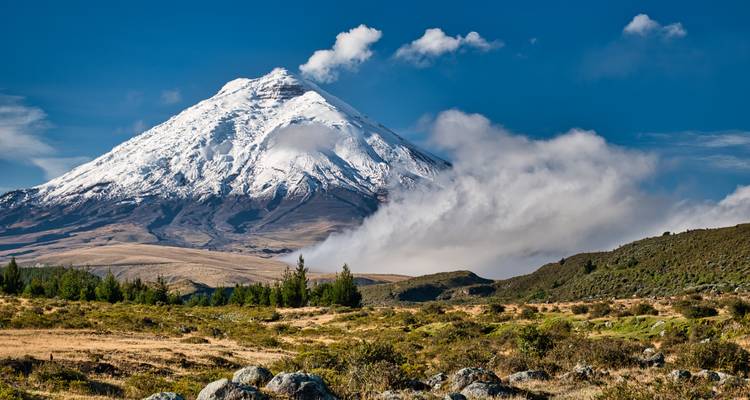 Snow-capped Cotopaxi Volcano towers above highland plains with swirling clouds around its slopes.