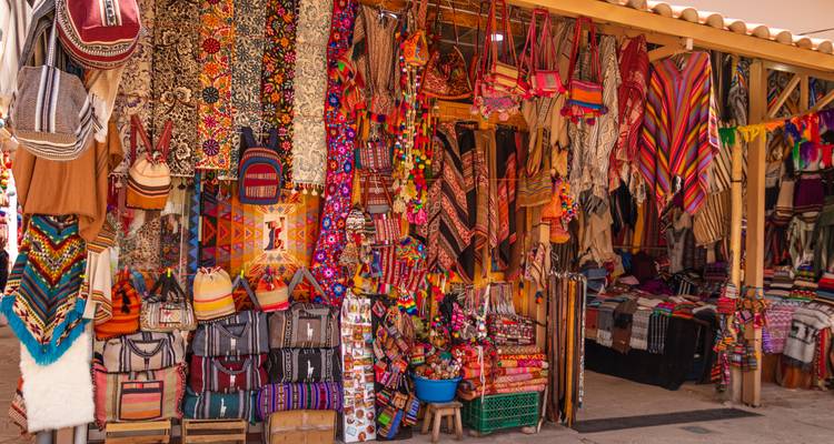 Vibrant outdoor market stall displaying a rainbow of woven textiles and bags in Peru.