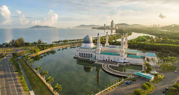 Mosquée blanche avec dôme bleu reflétée dans un lagon tranquille au lever du soleil avec l'horizon urbain au loin