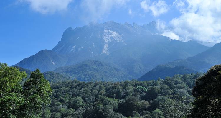 Pic de granit imposant du mont Kinabalu s'élevant au-dessus de la forêt tropicale dense sous des nuages épars