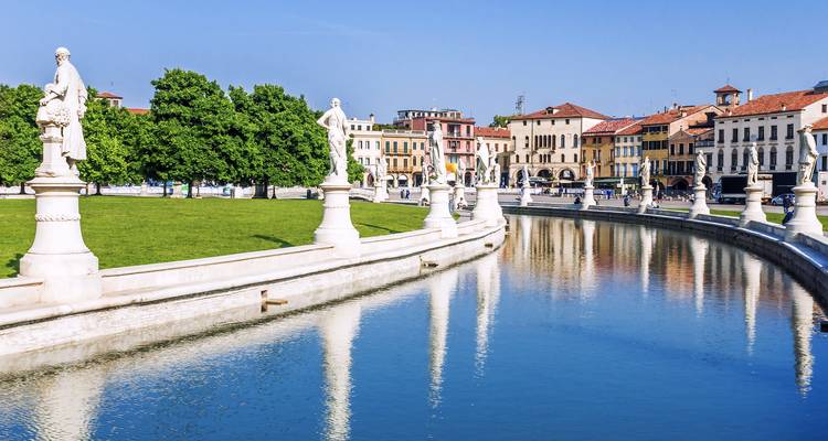 Statuengesäumter Kanal und gepflegte Rasenflächen des Prato della Valle, die einen klaren blauen Himmel in Padua widerspiegeln.