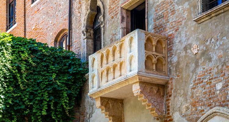 Der berühmte Balkon von Julia ragt aus einer von Grün bewachsenen Backsteinfassade in Verona hervor.