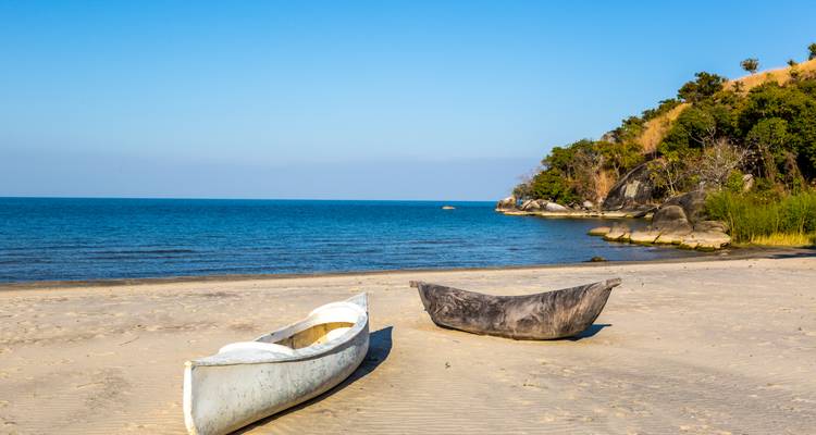 Zwei traditionelle Einbaumkanus ruhen an einem stillen Sandstrand neben dem ruhigen Malawisee.