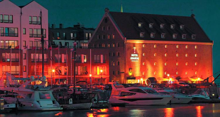 Blick auf einen Hafen mit einem Hotel und Yachten bei Nacht.