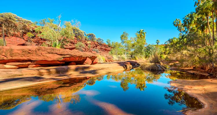 Reflective waterhole surrounded by red rocks.