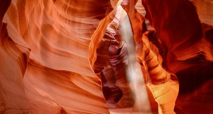 Paredes abstractas de arenisca serpenteante del Cañón del Antílope iluminadas por un haz de luz resplandeciente.
