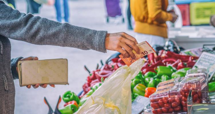 Ein Käufer reicht einen 10-Euro-Schein, um frische Paprika und Erzeugnisse an einem Marktstand im Freien zu kaufen