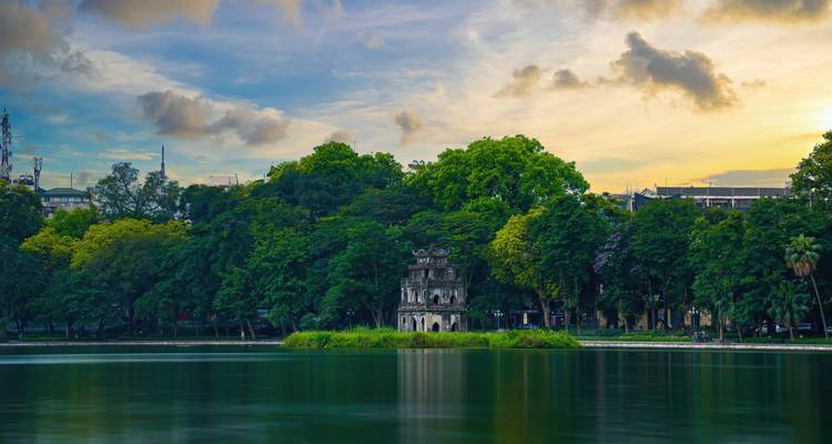 Historische toren op een meereiland te midden van dicht groen gebladerte.