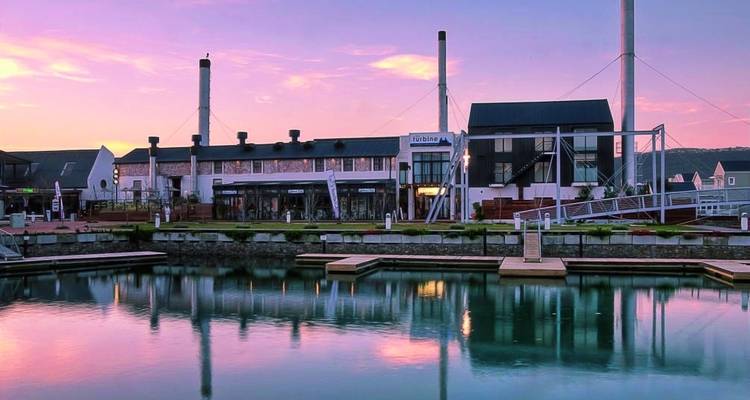 Modern waterfront buildings with reflections in a lake at dusk.