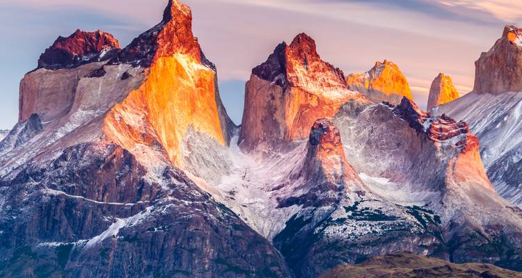 Sunlit Cuernos del Paine peaks dusted with snow glowing at sunrise against pastel skies