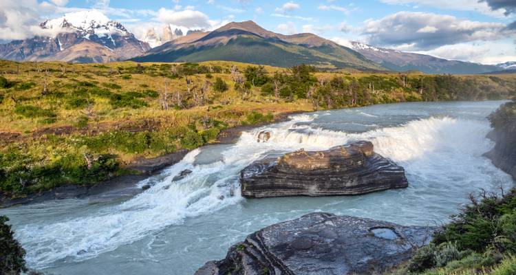 Powerful waterfall cascading through rugged Patagonian landscape with snowy peaks in the distance