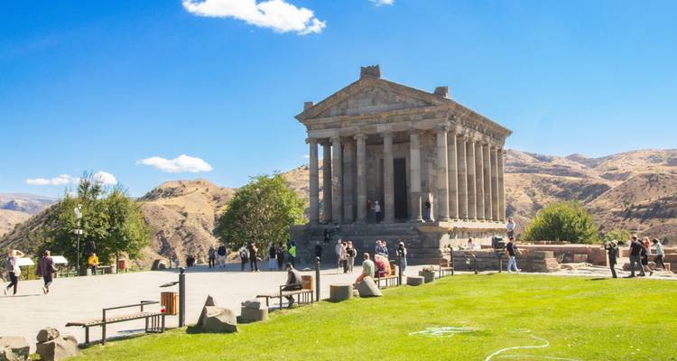Touristen erkunden das Garni-Tempel-Plateau mit umgebenden Bergen und blauem Himmel.