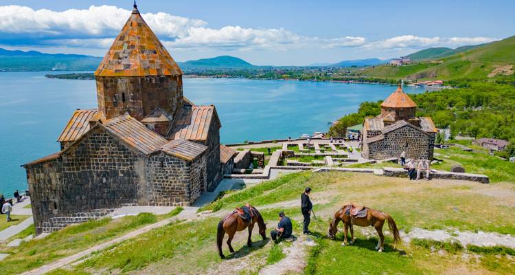 Sevanavank-Klöster mit Blick auf den blauen Sewansee mit Pferden und Reitern im Vordergrund.