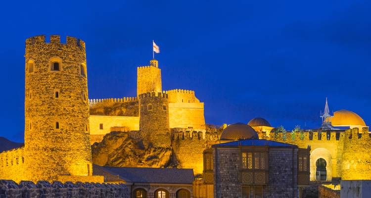 Nachtansicht der beleuchteten Steinmauern und des Turms der Rabati-Festung mit Nationalflagge.
