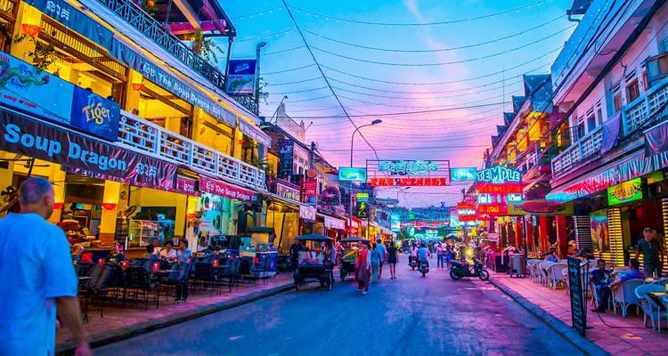 Scène de rue animée avec des enseignes illuminées et une vie nocturne intense.