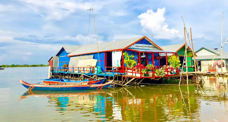 Maisons colorées sur pilotis au-dessus d'un lac avec des reflets sur l'eau.