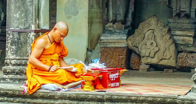 Monnik in oranje gewaden zittend, omringd door tempelbeeldhouwwerken.