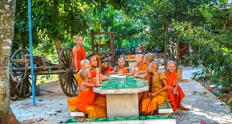 Jonge monniken in oranje gewaden zittend aan een tafel buiten.