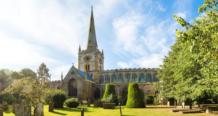 Church with tall spire in green surroundings.