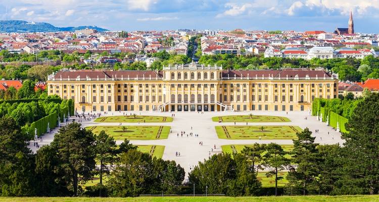 A grand palace with gardens in front, surrounded by a cityscape.
