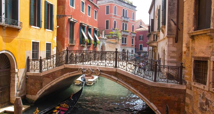 Venice canal with a gondola passing under a bridge.