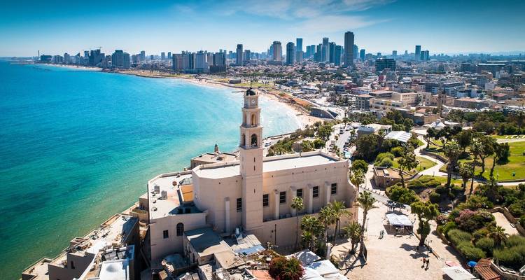 Vista aérea de una ciudad costera con una torre de iglesia prominente y edificios modernos.