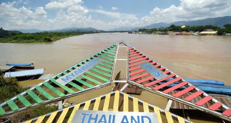 Dreieckiges Bootsdach, bemalt mit Myanmar-, Laos- und Thailand-Motiven, das auf ein schlammiges Mekong-Fluss-Panorama zeigt.