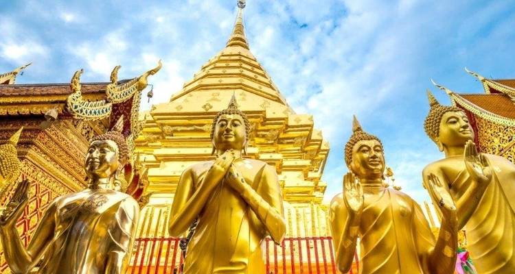 Goldene Buddha-Statuen in einer Tempelanlage mit leuchtend buntem Himmel.