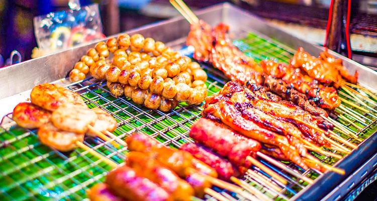 Étal de nourriture de rue avec viande grillée et saucisses.