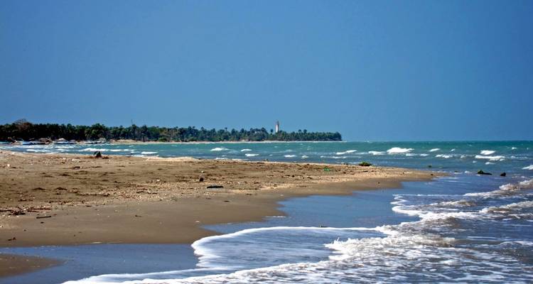 Een strand met golven die zacht aanslaan en een vuurtoren zichtbaar in de verte.