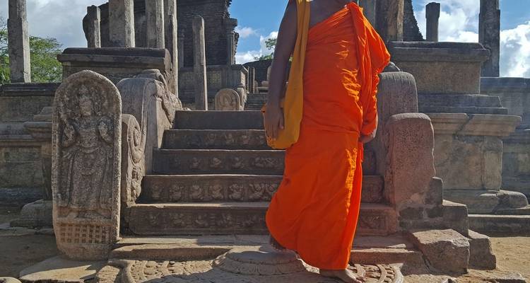 Een monnik in een oranje gewaad die wandelt nabij oude steengravures.