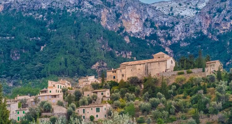 Un village à flanc de colline avec des bâtiments en pierre entourés d'une végétation luxuriante et de montagnes.
