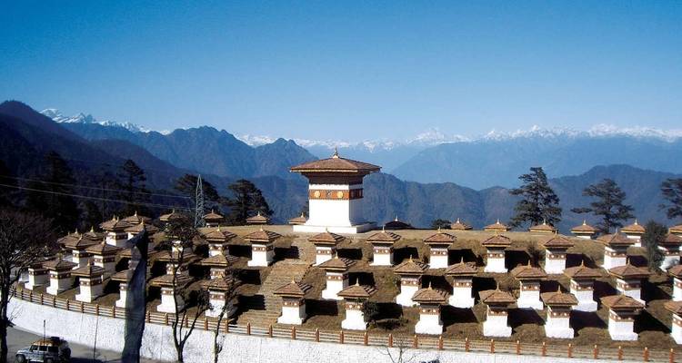 A row of stupas in Bhutan with mountains in the background.