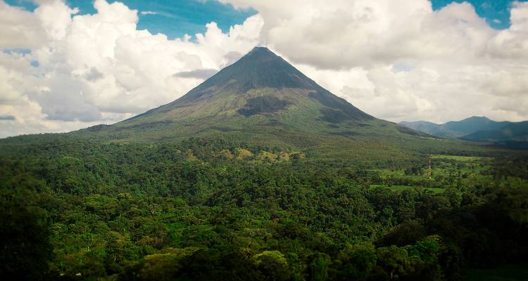 El icónico Volcán Arenal se eleva sobre la densa selva tropical con nubes flotando alrededor de la cumbre.