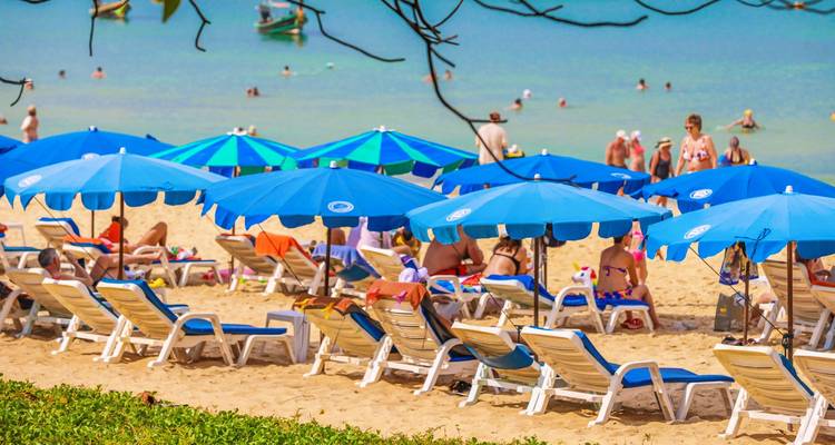 Una escena de playa concurrida con sombrillas coloridas y personas relajándose junto al mar.