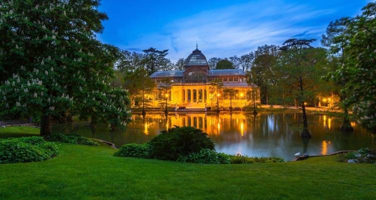 Un hermoso edificio de cristal iluminado reflejado en un estanque tranquilo al anochecer.