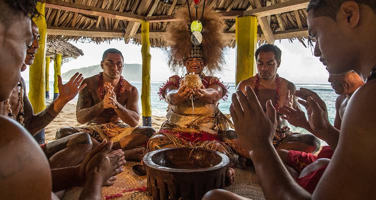Cultural ceremony with people in traditional attire sitting in a circle inside a thatched structure.