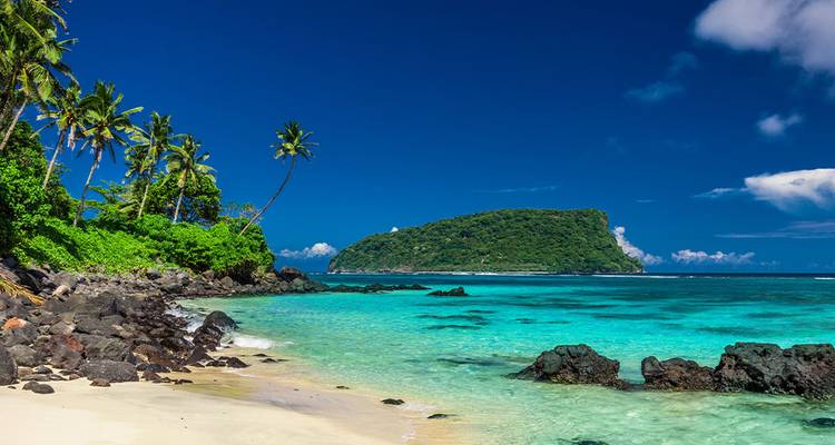Clear blue tropical waters with lush greenery and a distant island.