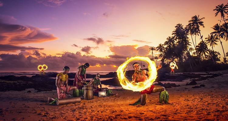 People performing traditional fire dance on the beach at sunset.