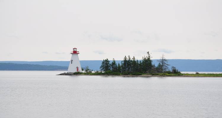 A picturesque lighthouse on a small island against a calm sea.
