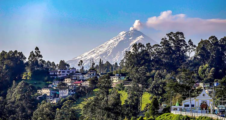 Uitzicht op de vulkaan Cotopaxi met een rookpluim boven een dorp.